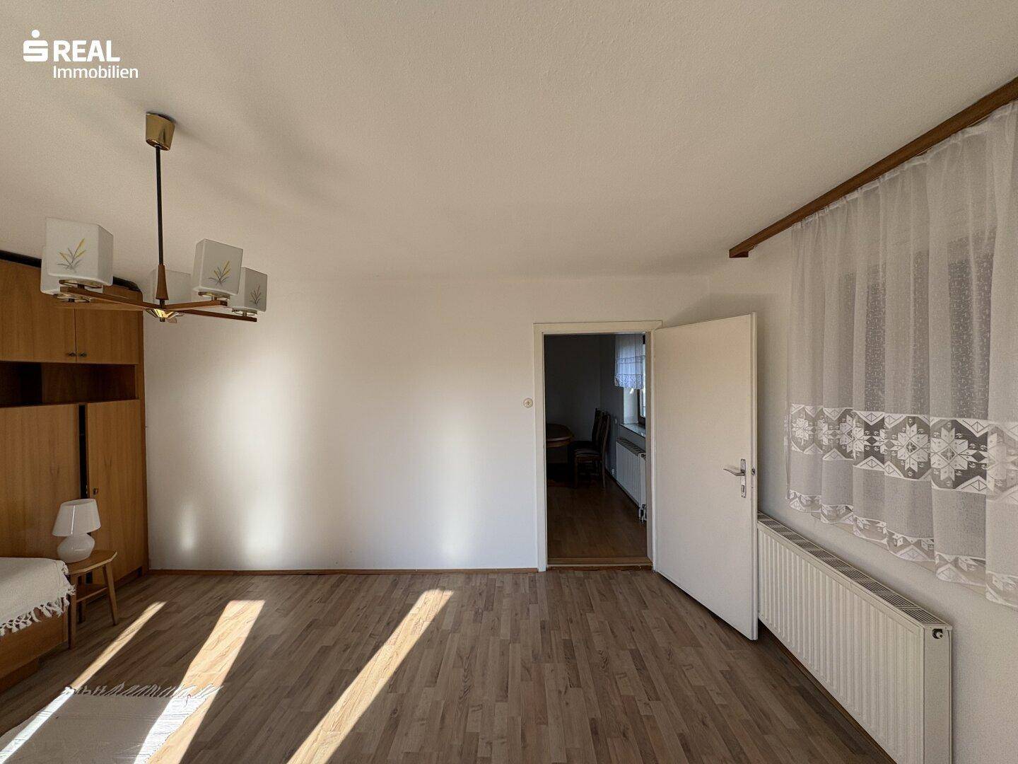 Helles Schlafzimmer mit Laminatboden und Zugang zu einem weiteren Raum, gut beleuchtet.