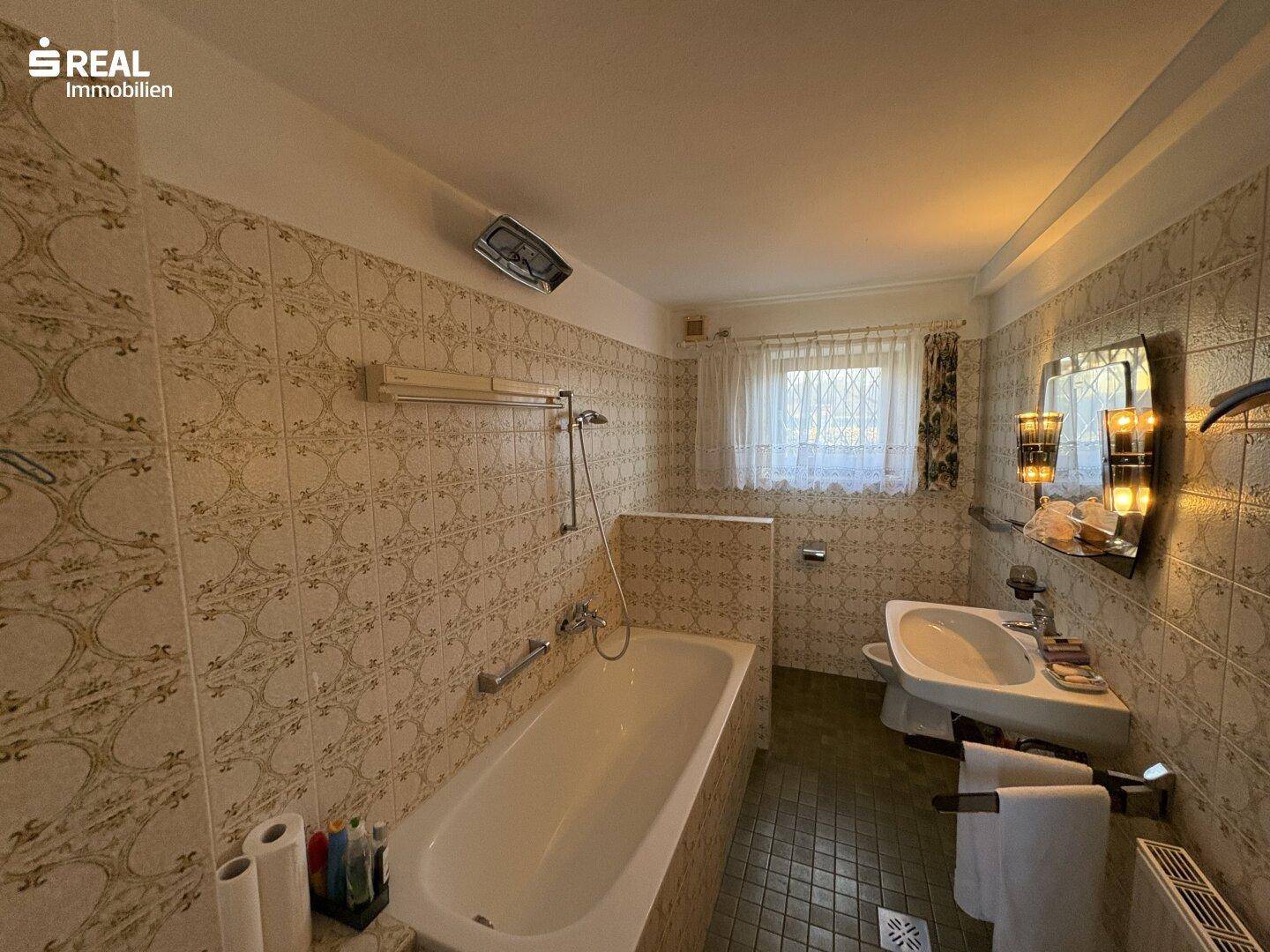 Badezimmer im Stil der 80er Jahre mit Badewanne, Waschbecken und gemusterten Fliesen.