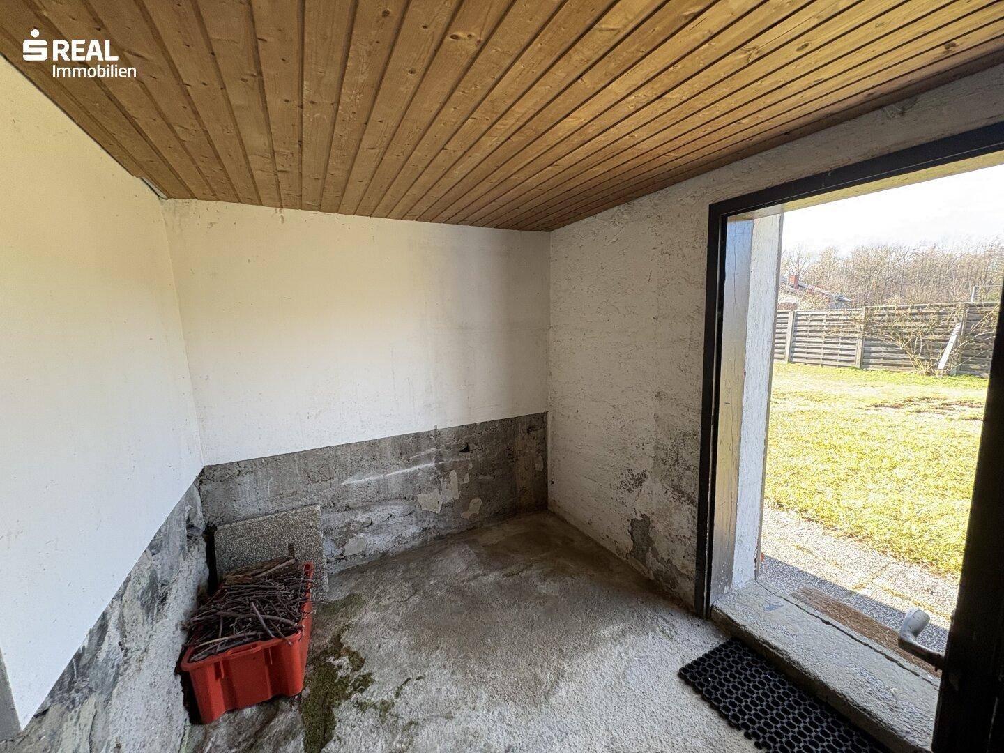 Einfacher Abstellraum mit Betonboden und Zugang zum Garten, praktisch und funktional.