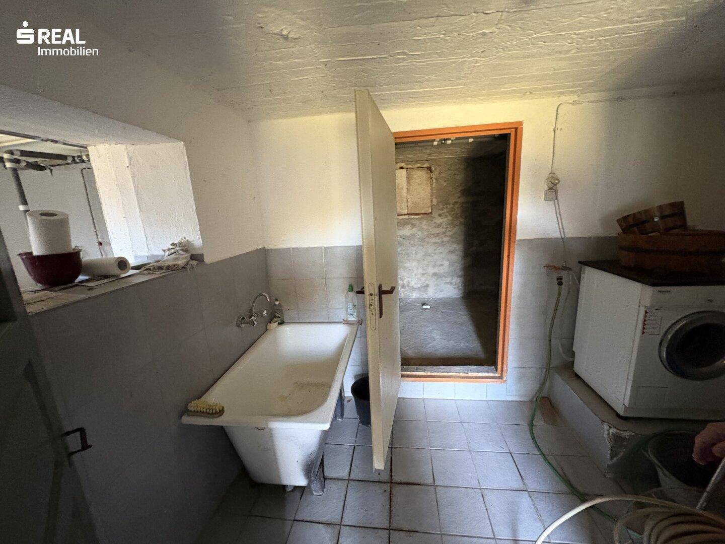 Kellerraum mit Badewanne, Waschmaschine und Fliesenboden, als Waschküche nutzbar.
