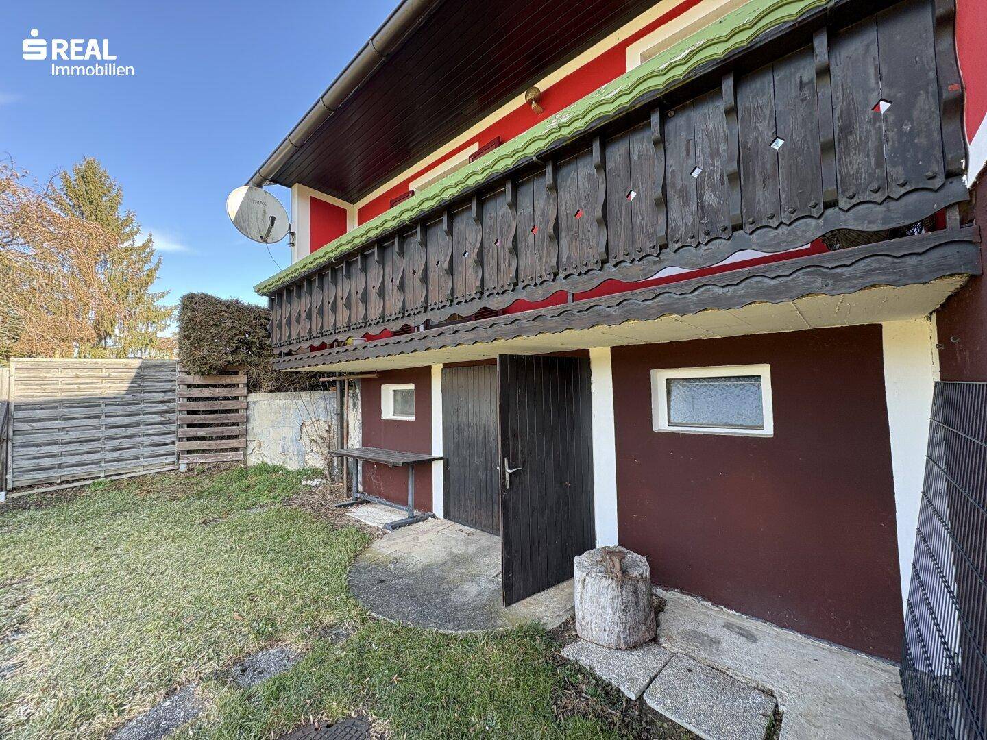 Seitenansicht des Hauses mit Holzbalkon und Zugang zur Rasenfläche.