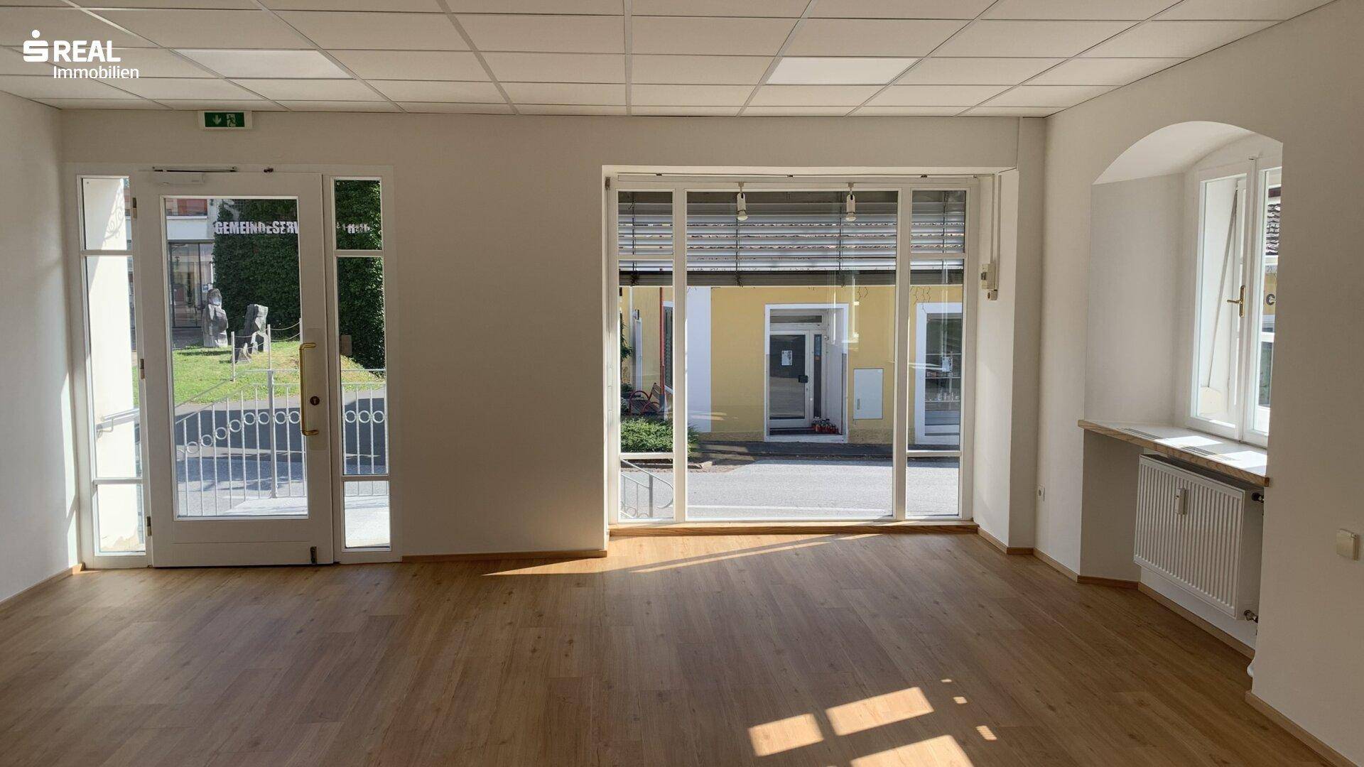 Heller, leerer Gewerberaum mit großen Fenstern, Holzboden und viel Tageslicht, bereit zur Nutzung.