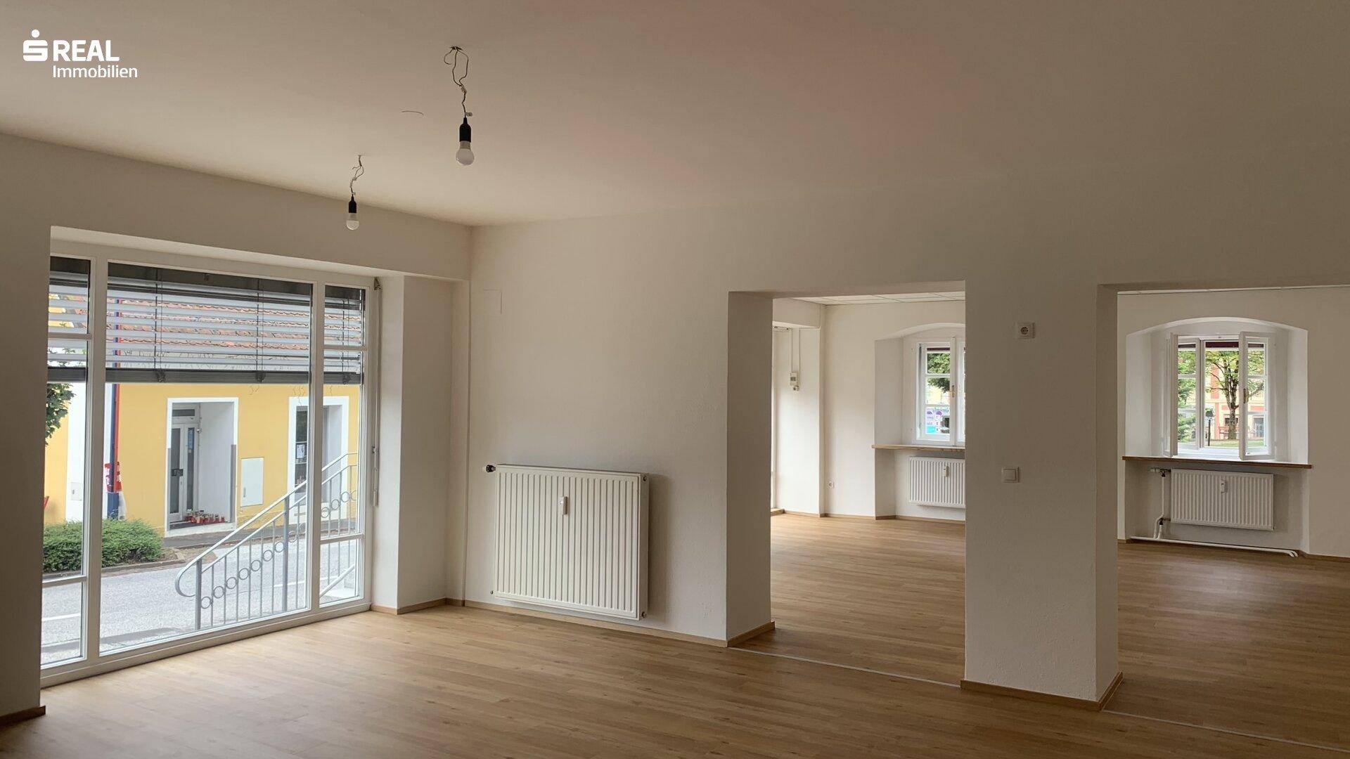 Geräumiger, heller Gewerberaum mit großen Fenstern, Heizkörpern und Holzboden, ideal für verschiedene Zwecke.