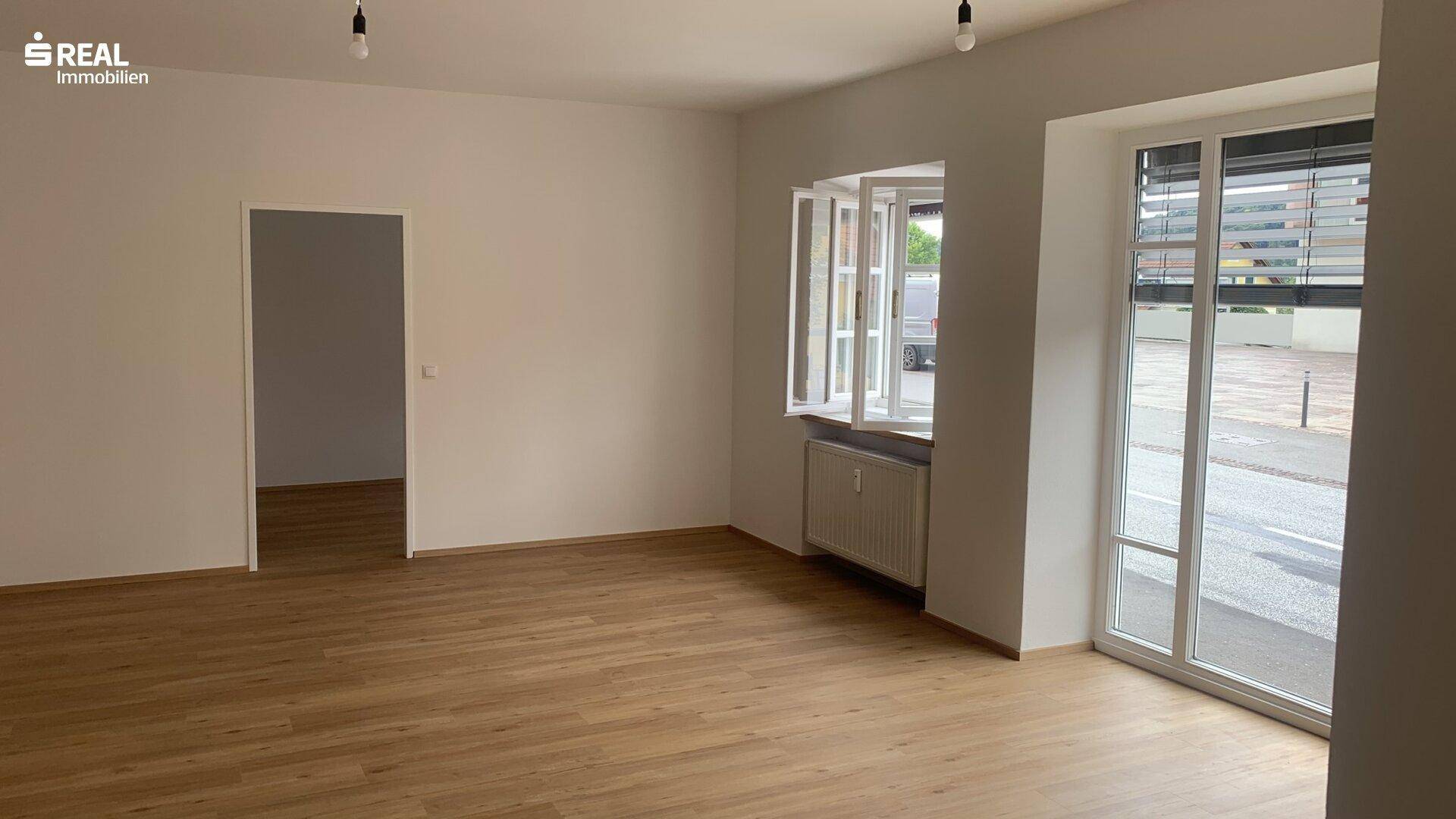Leerer Gewerberaum mit großen Fenstern, Holzboden und Zugang zu weiteren Räumen, sehr gepflegt.