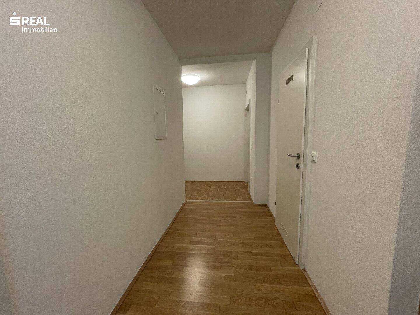 Langer Flur mit Holzboden und weißen Wänden, der zu weiteren Räumen führt.