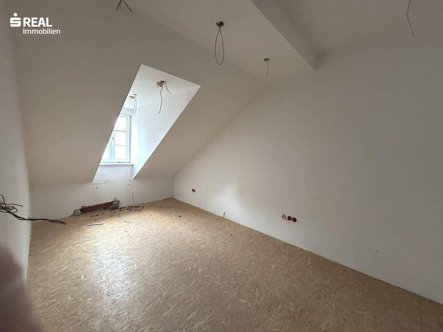 Dachgeschossraum in Renovierung mit schrägen Wänden und einem Dachfenster, bereit für den Ausbau.