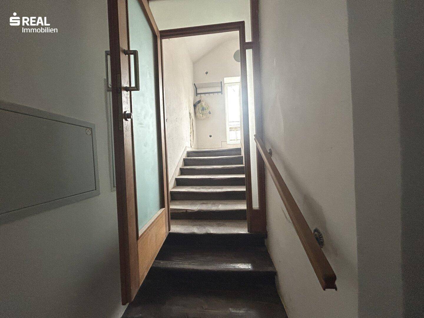 Treppenaufgang mit Holztür und Handlauf, der zu weiteren Stockwerken führt.