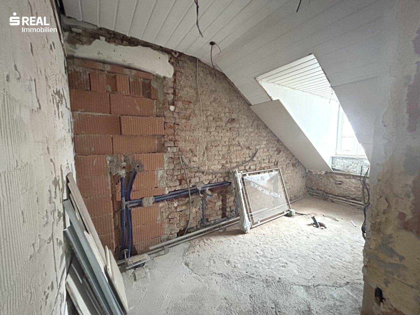 Raum in Rohbauweise mit freiliegenden Ziegelwänden und Installationen, bereit für den Ausbau.