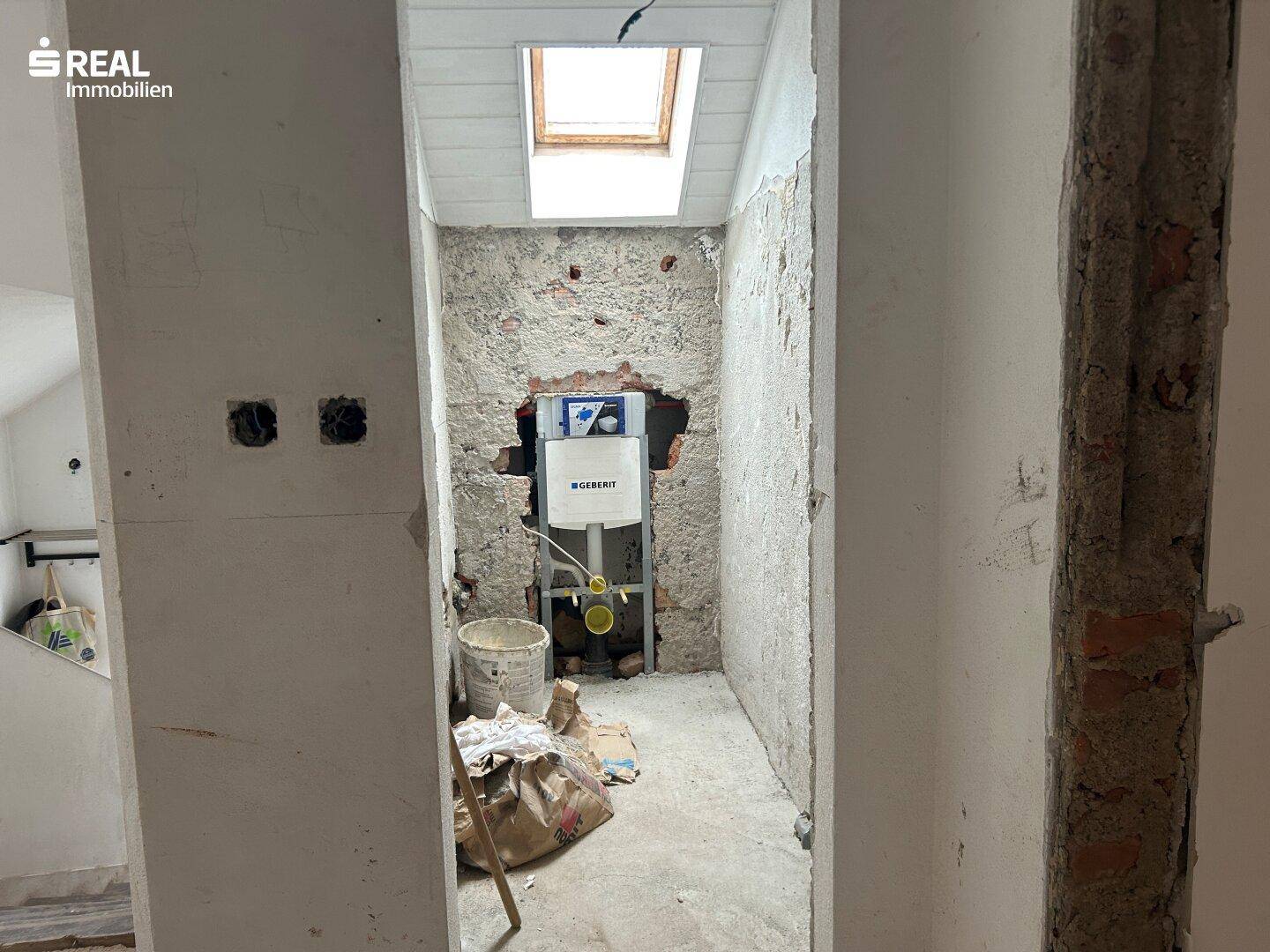Kleiner Raum in Rohbauweise mit Vorinstallation für Toilette und einem Dachfenster.