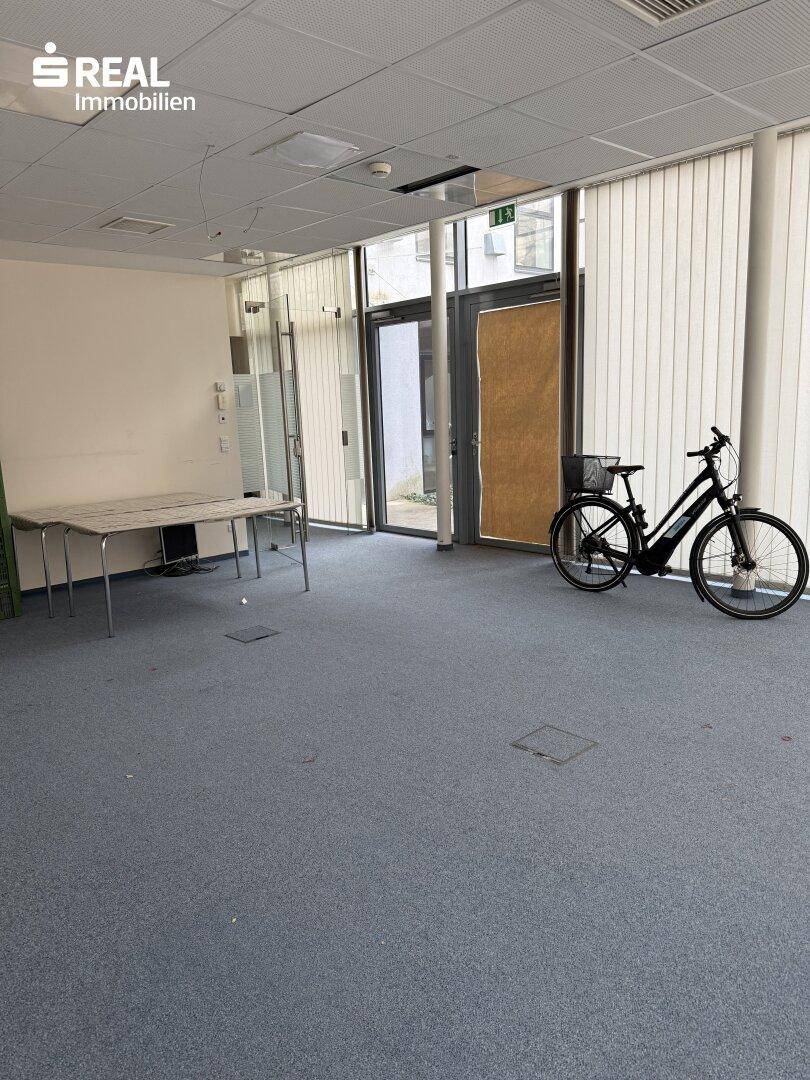 Großes Büro mit Teppichboden, Glastür und einem Fahrrad im Raum.