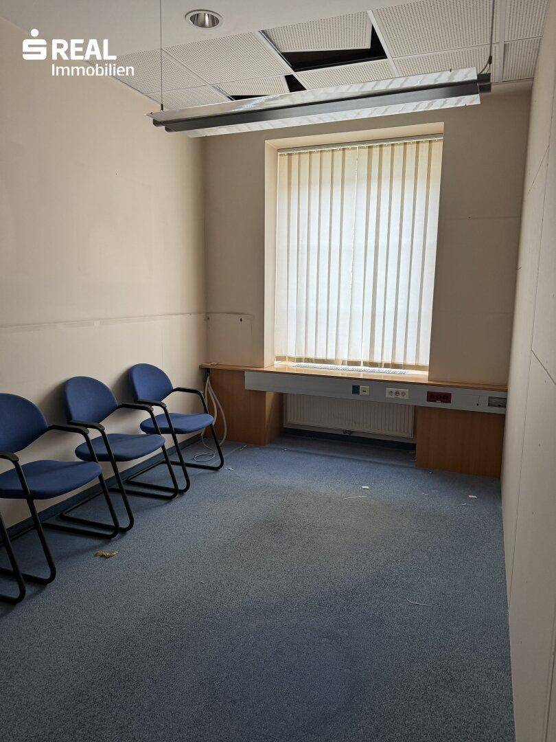 Büro mit Teppichboden, Fenster und blauen Stühlen, bereit für Besprechungen.