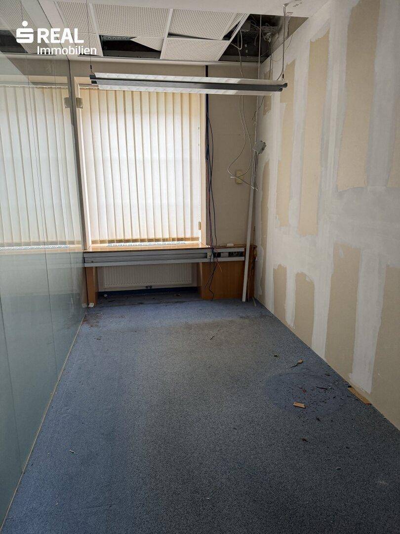 Kleineres Büro mit Teppichboden, Fenster und einer Arbeitsplatte unter dem Fenster.