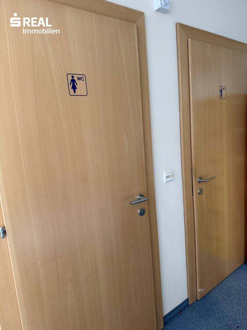 Flur mit zwei Holztüren, gekennzeichnet als Toiletten für Damen und Herren.