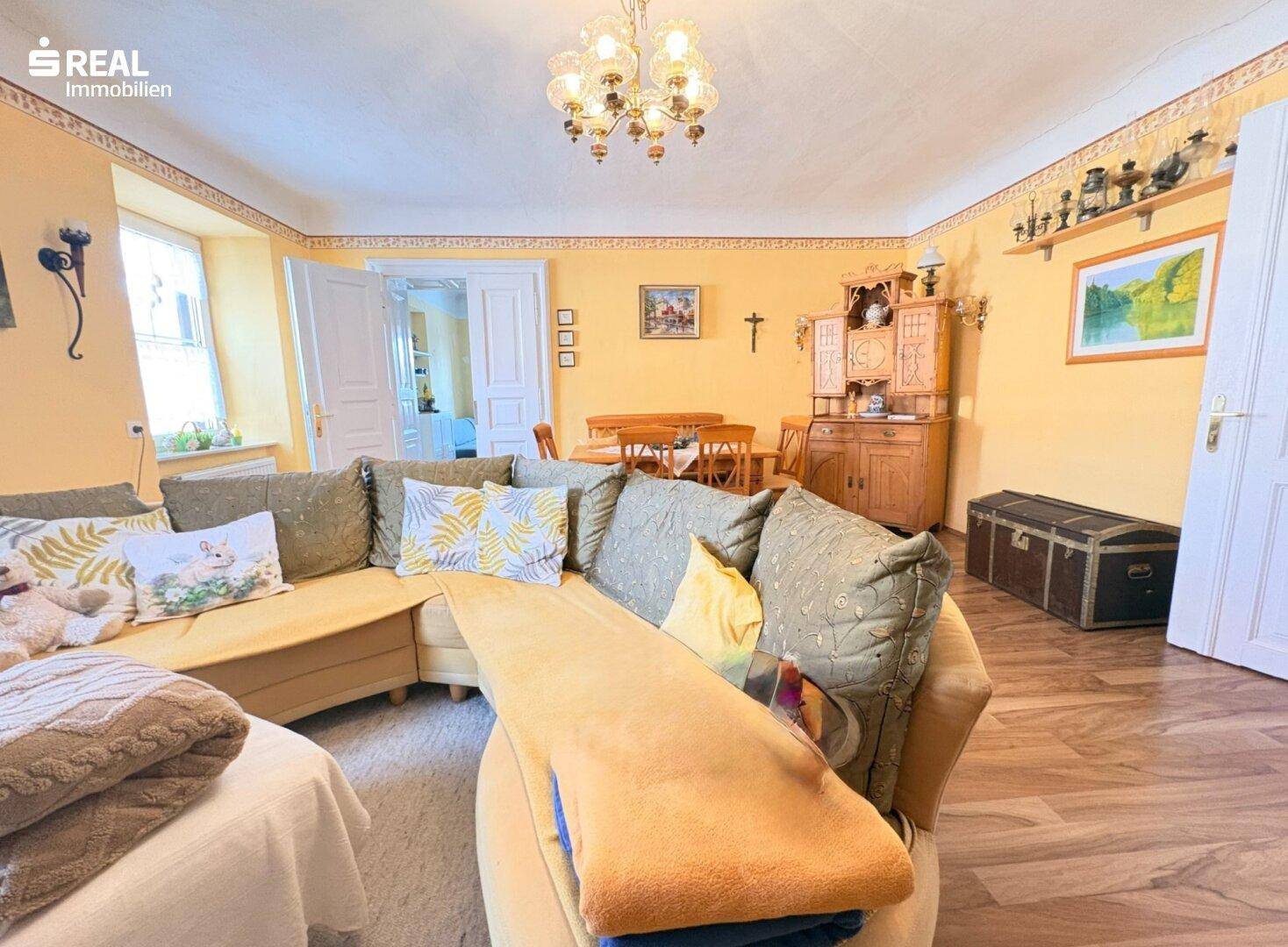 Gemütliches Wohnzimmer mit großem Ecksofa, traditionellem Kronleuchter und Holzboden.