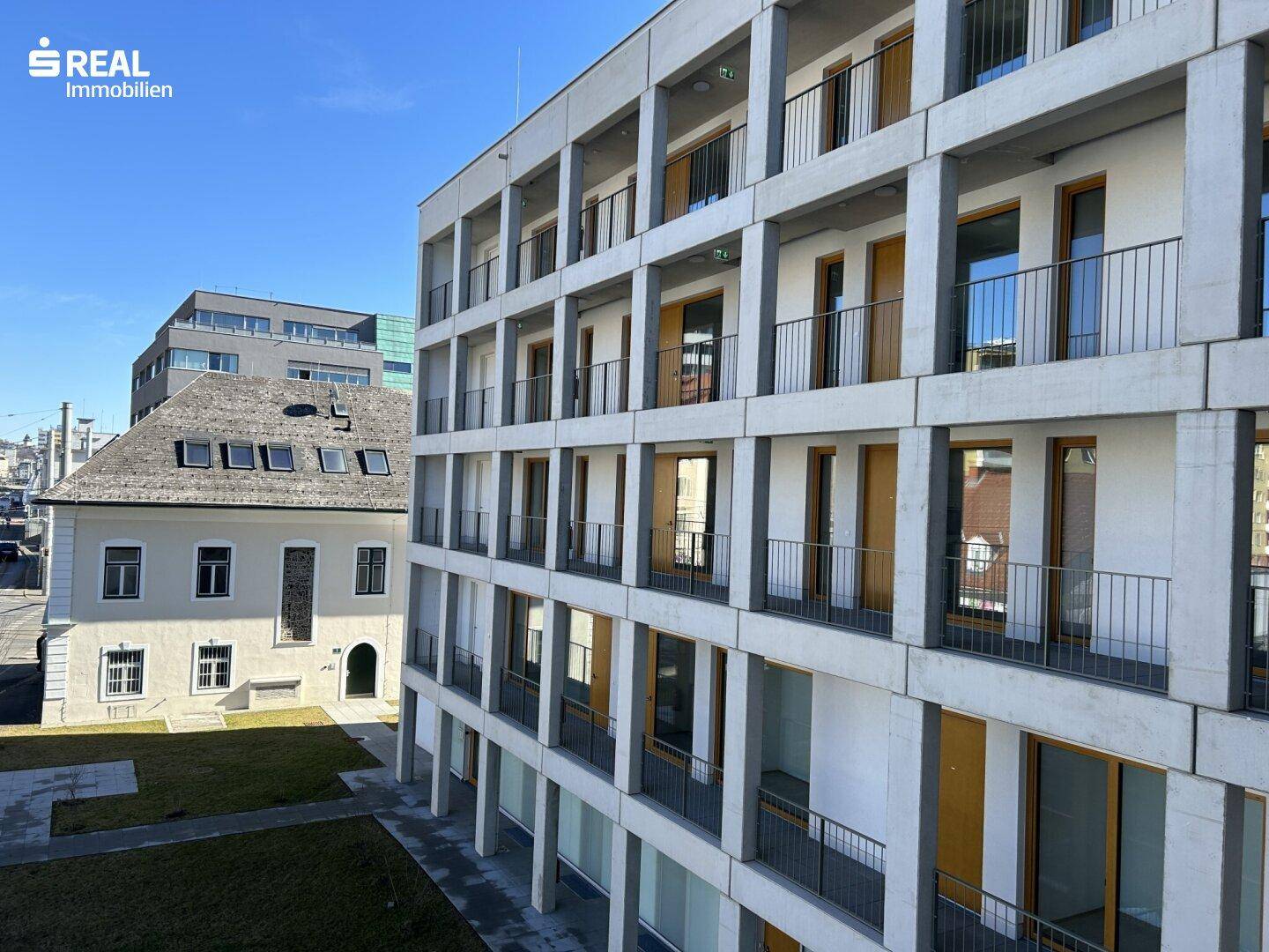 Ansicht der modernen Gebäudefassade mit Balkonen und angrenzendem historischen Altbau.