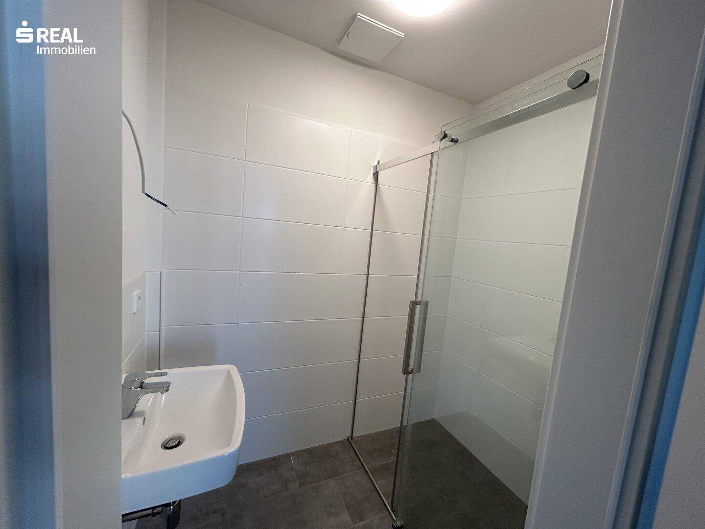 Modernes Badezimmer mit Duschkabine, Waschbecken und weißen Wandfliesen.