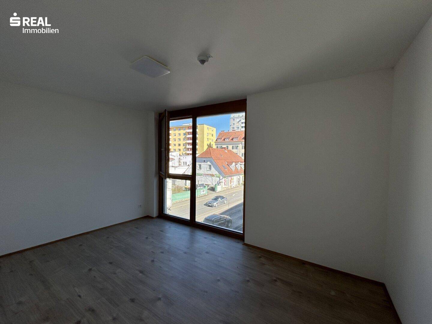 Geräumiges, helles Zimmer mit Laminatboden und großem Fenster mit Blick auf die Umgebung.