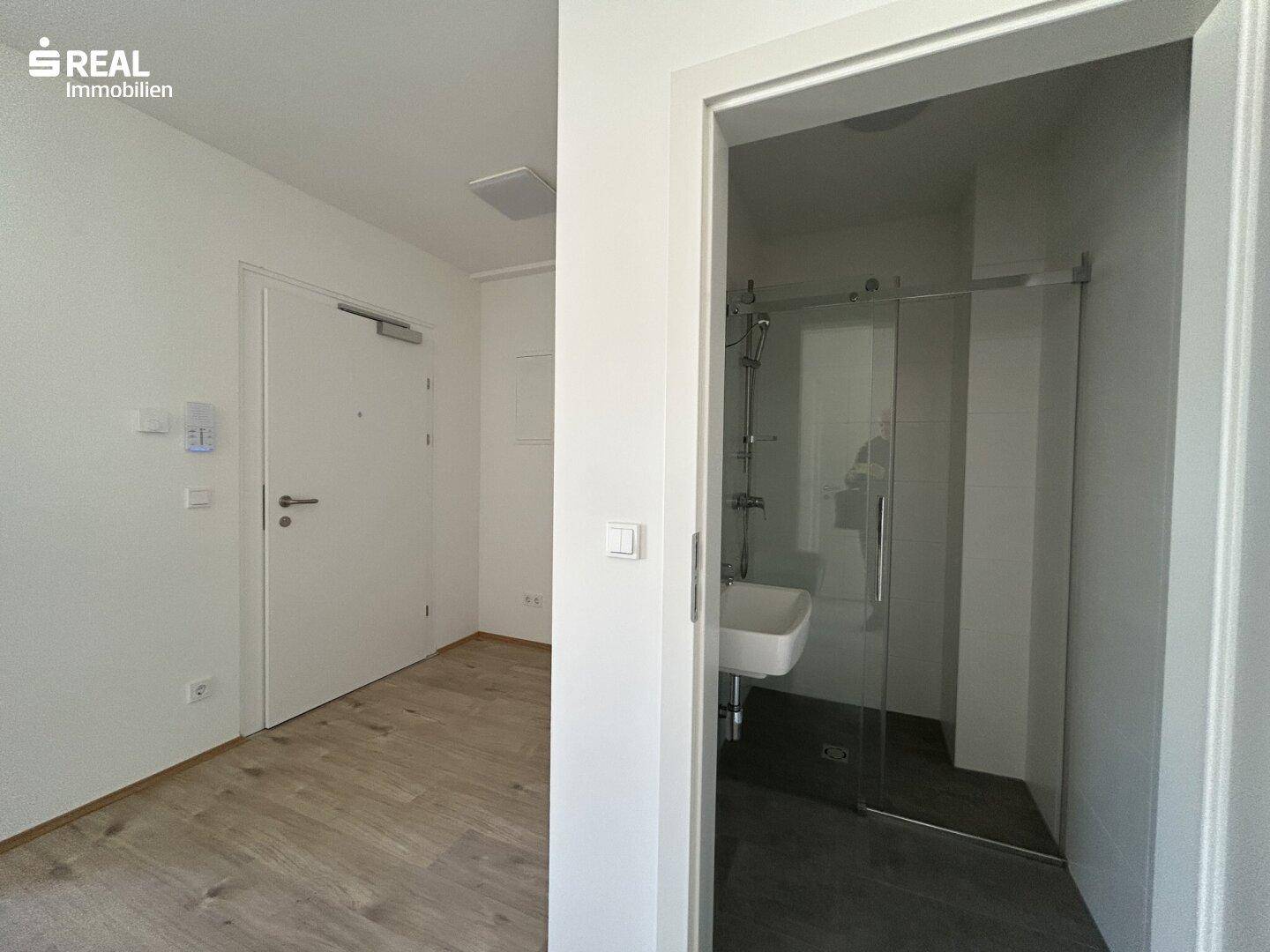 Eingangsbereich mit Laminatboden und Blick in das moderne Duschbad.