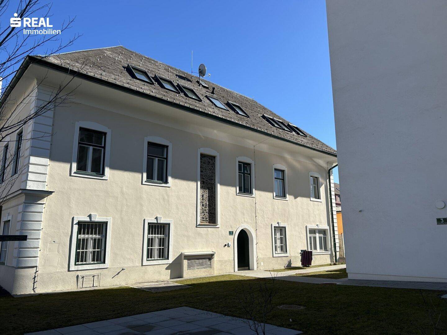 Historisches Gebäude mit klassischer Fassade und begrüntem Vorgartenbereich.