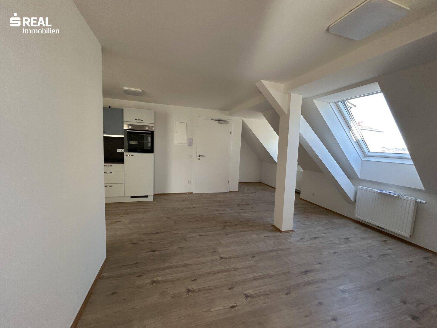 Helles Dachgeschosszimmer mit Küchenzeile, Laminatboden und Dachfenster.