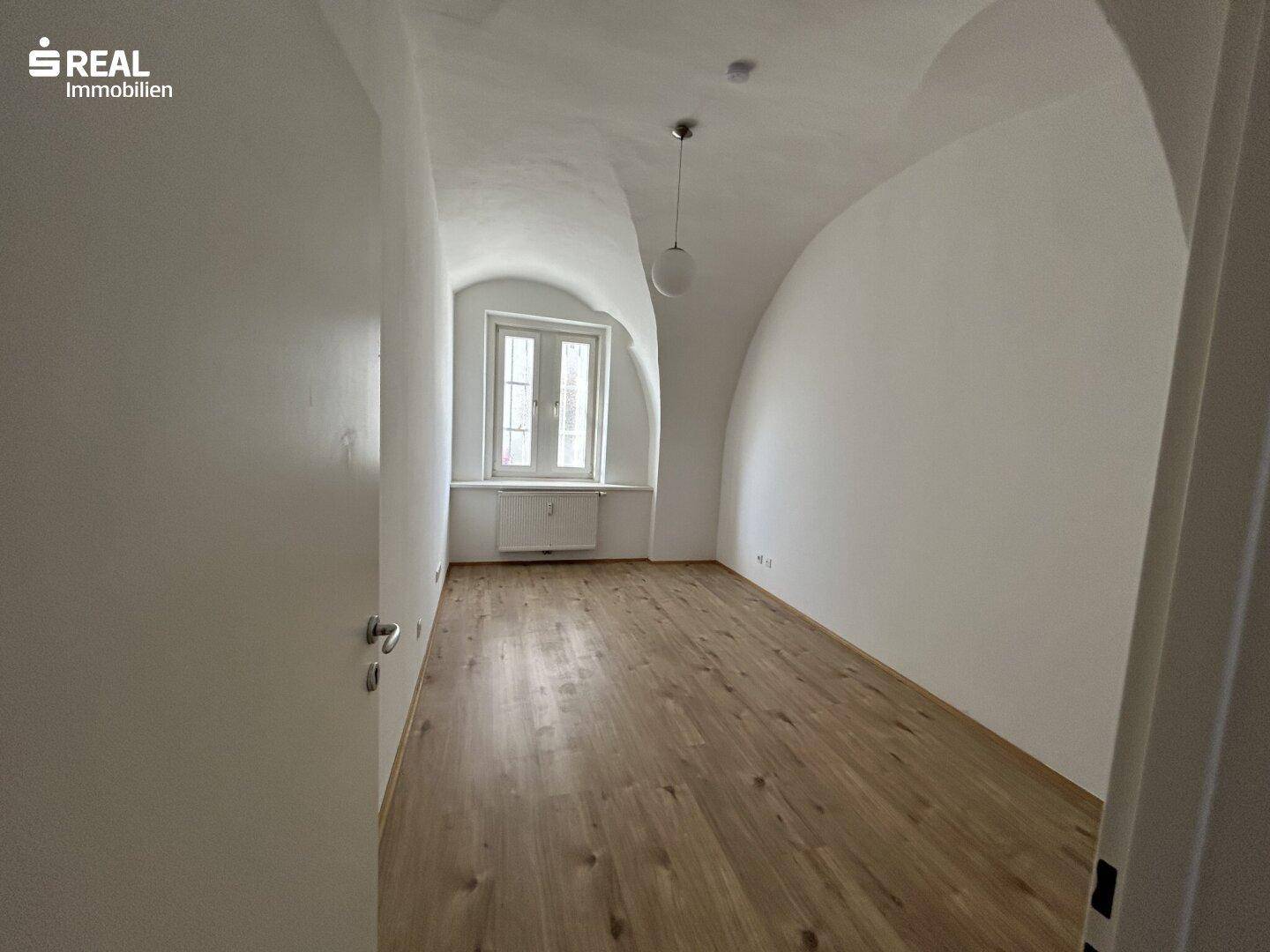 Geräumiges Zimmer mit Laminatboden, Gewölbedecke und Fenster mit Stadtblick.