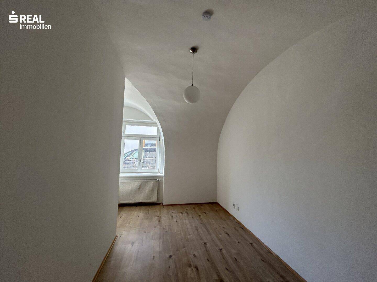 Geräumiges Zimmer mit Laminatboden, Gewölbedecke und natürlichem Lichteinfall.
