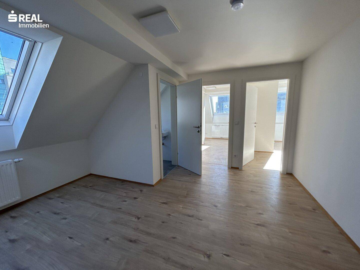 Helles Dachgeschosszimmer mit Laminatboden, Dachschrägen und offenen Türen.