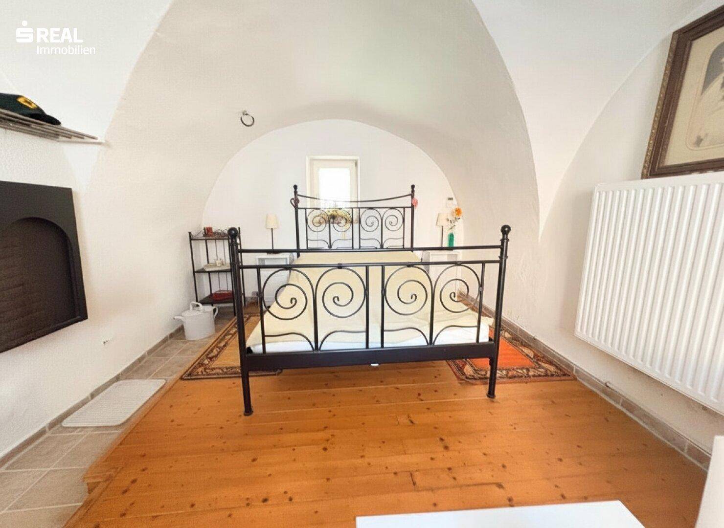 Gemütliches Schlafzimmer mit beeindruckender Gewölbedecke, Holzboden und einem schmiedeeisernen Bett.