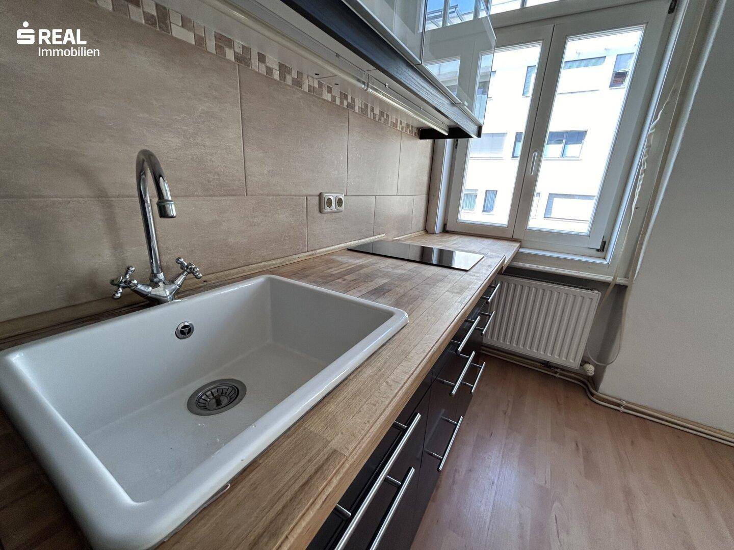 Detailansicht der Küchenzeile mit Spüle, Holz-Arbeitsplatte und Induktionskochfeld am Fenster.