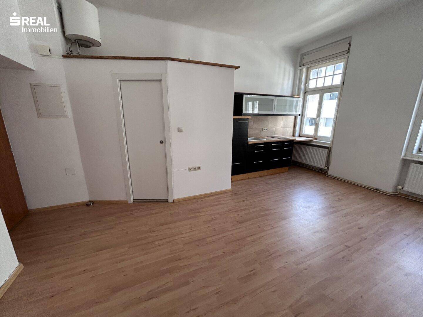 Heller Wohnraum mit Parkettboden und integrierter Küchenzeile, ideal für ein Studio-Apartment.