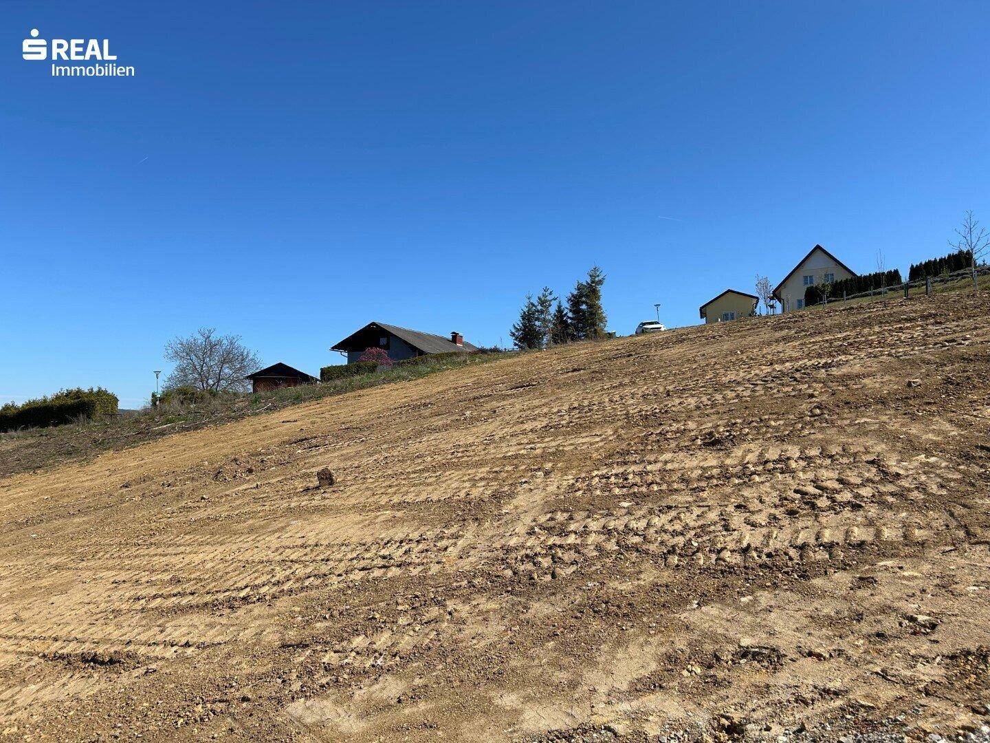 Hanglage des Baugrundstücks mit Blick auf die oberen Häuser und den klaren Himmel.