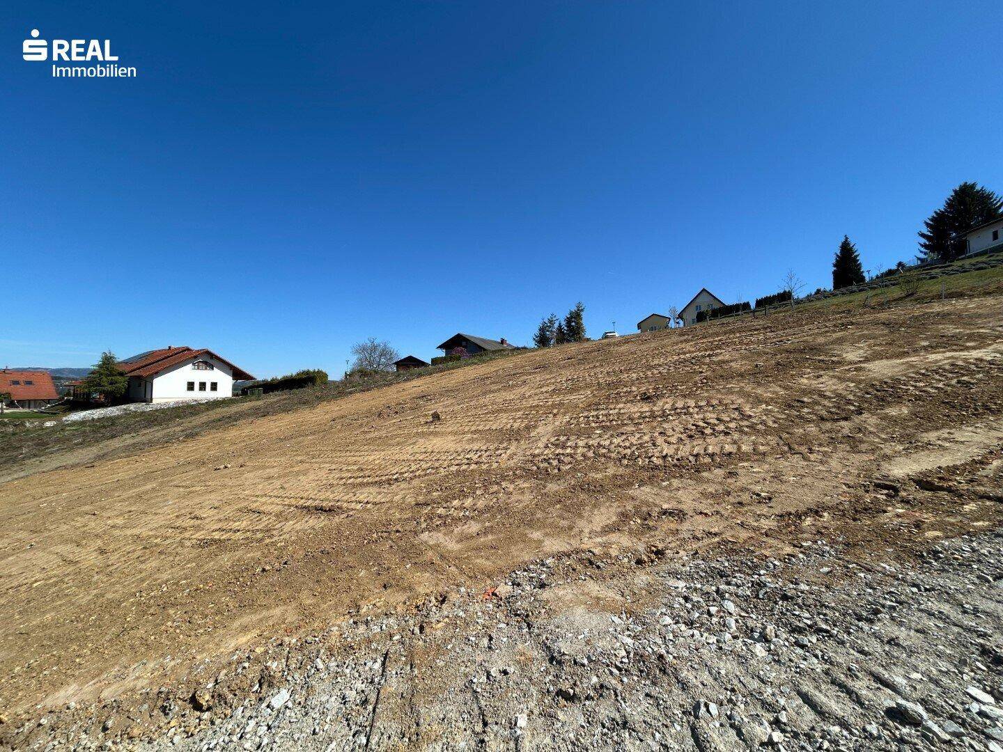 Baugrundstück in Hanglage mit Schotterfläche und weitem Blick auf die Berglandschaft.