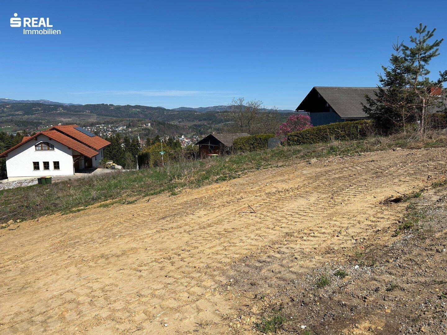 Blick über das Grundstück mit angrenzenden Häusern und hügeliger Landschaft im Hintergrund.