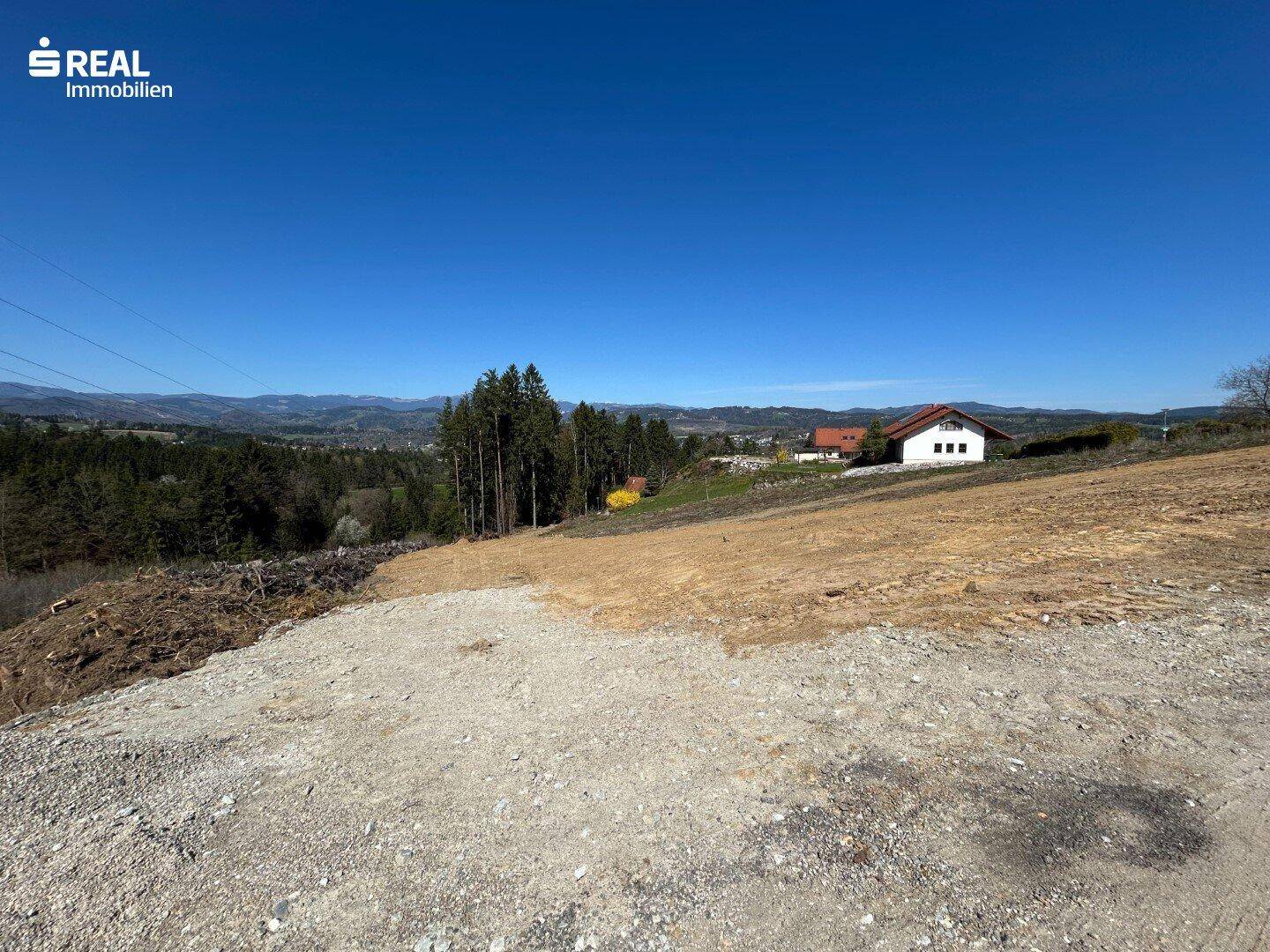 Großes, sonniges Grundstück mit freiem Blick auf die bewaldete Landschaft und die Berge.