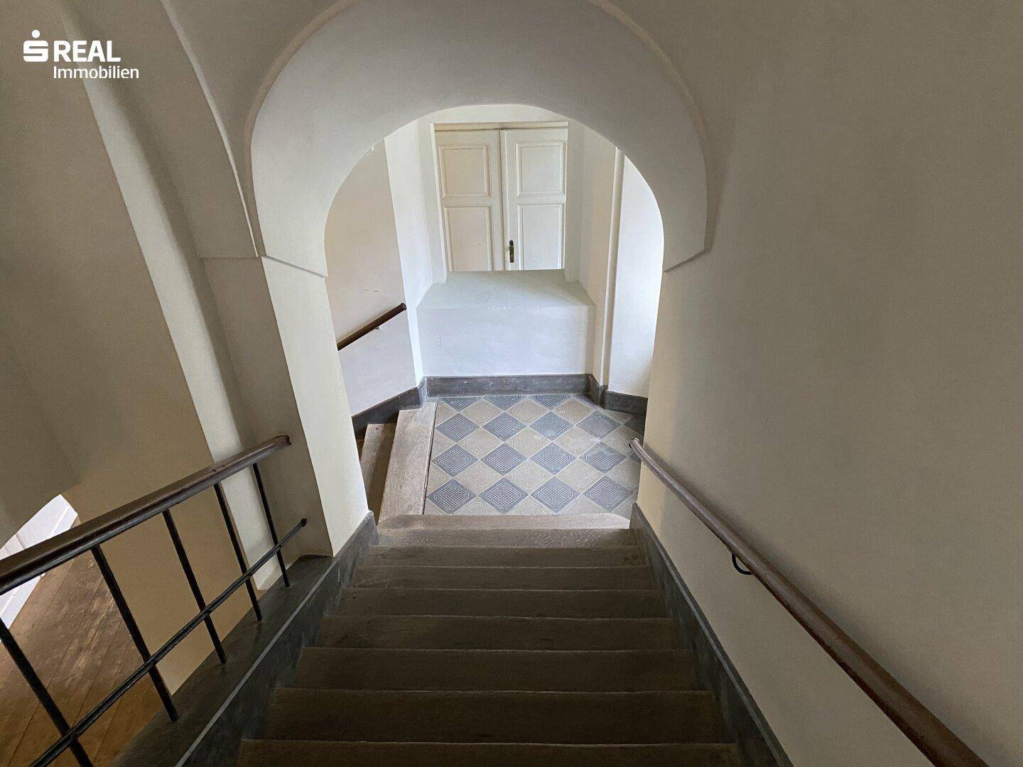 Historisches Treppenhaus mit gewölbter Decke und kariertem Fliesenboden in einem Altbau.