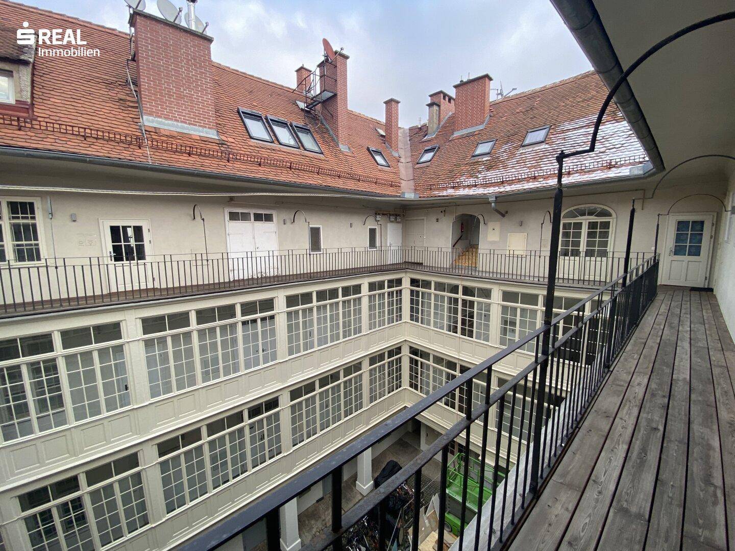Historischer Innenhof mit umlaufenden Holzgalerien und roten Ziegeldächern unter bewölktem Himmel.
