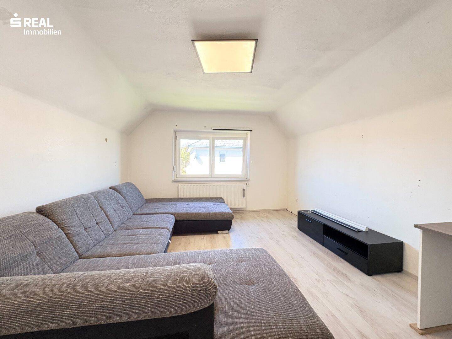 Geräumiges Wohnzimmer im Dachgeschoss mit großem Sofa und Laminatboden.