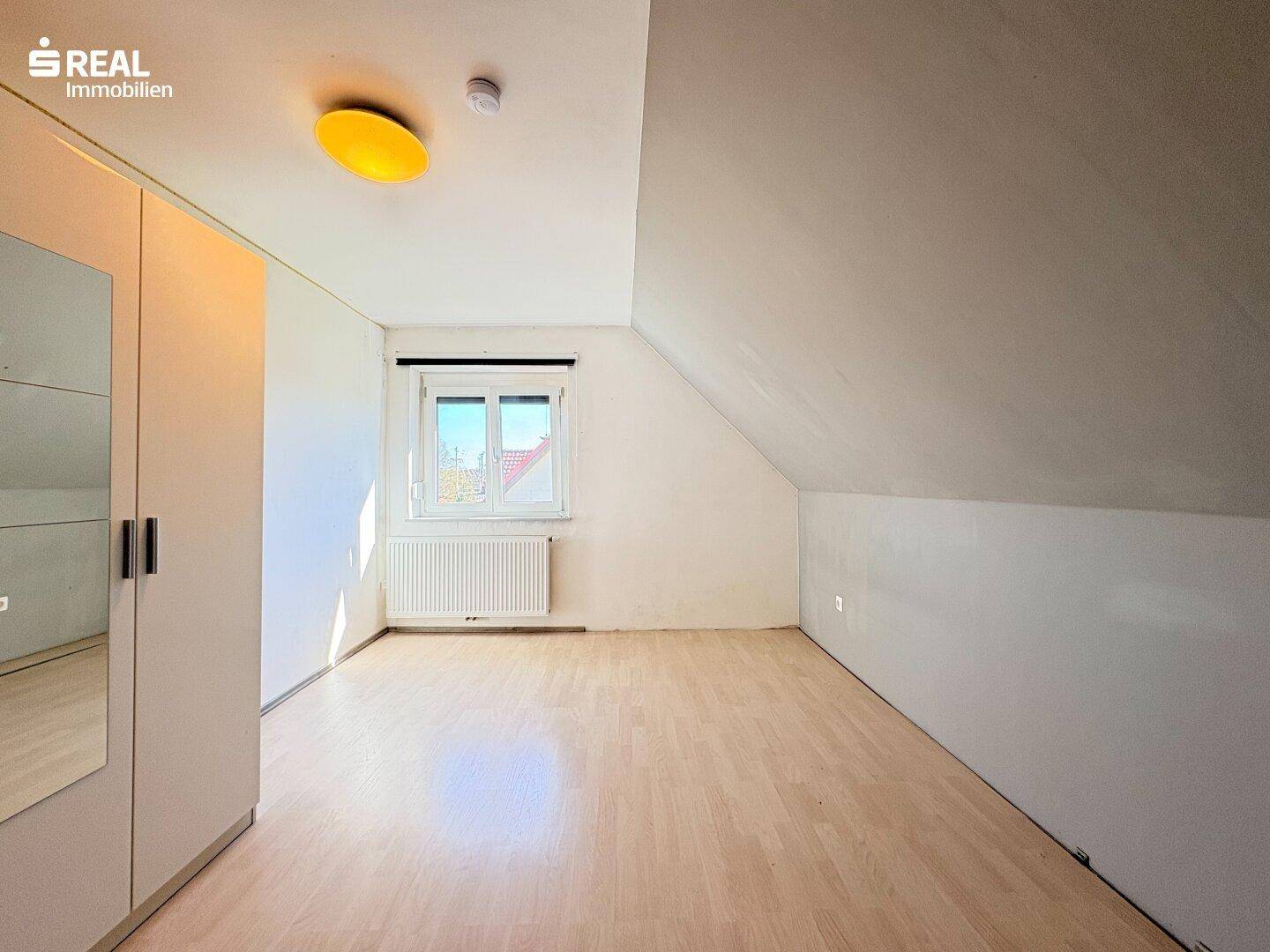 Schlafzimmer im Dachgeschoss mit Laminatboden, Kleiderschrank und schrägen Wänden.