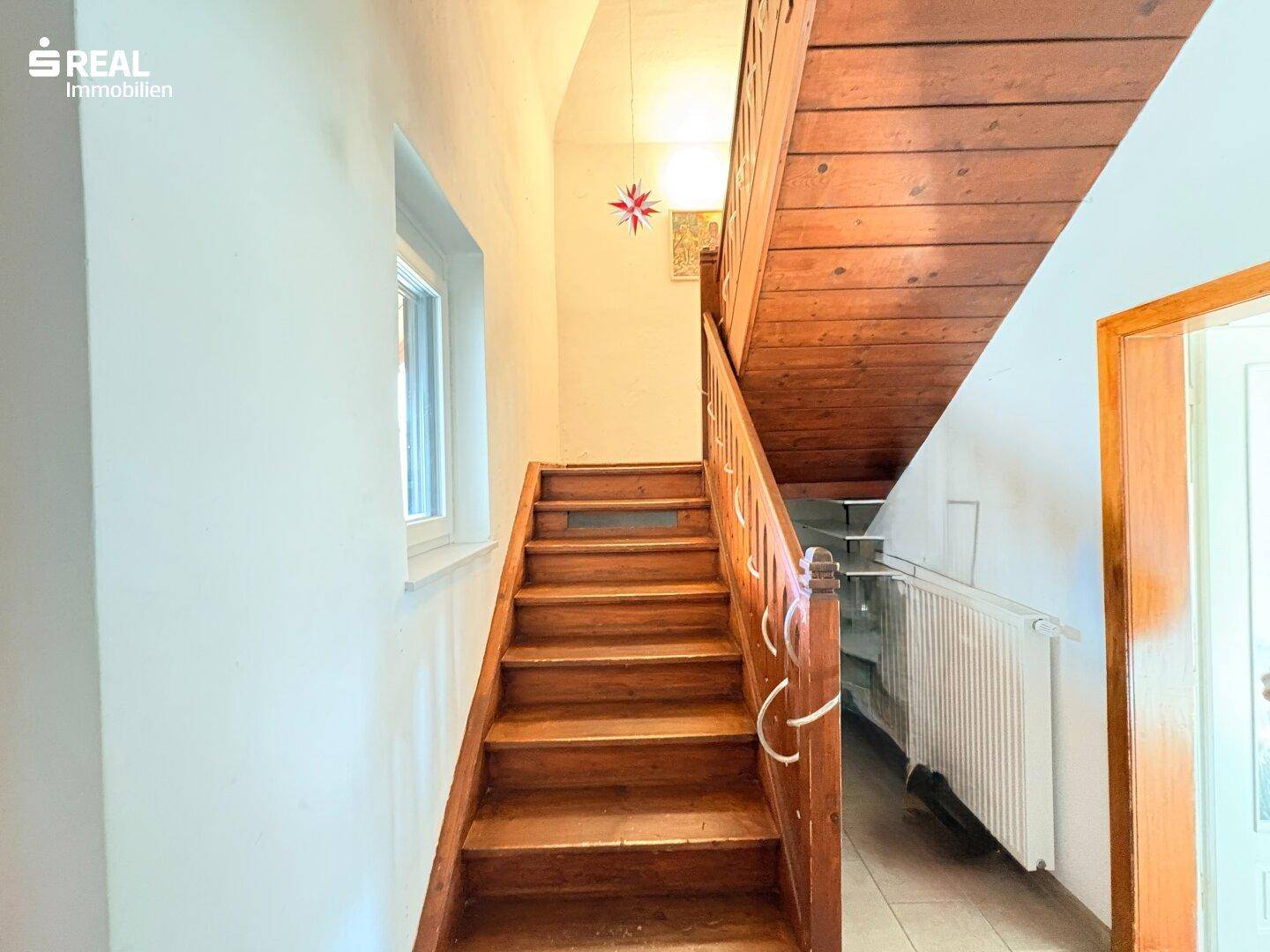 Holztreppe führt in die oberen Stockwerke, mit Fenster für natürliches Licht.