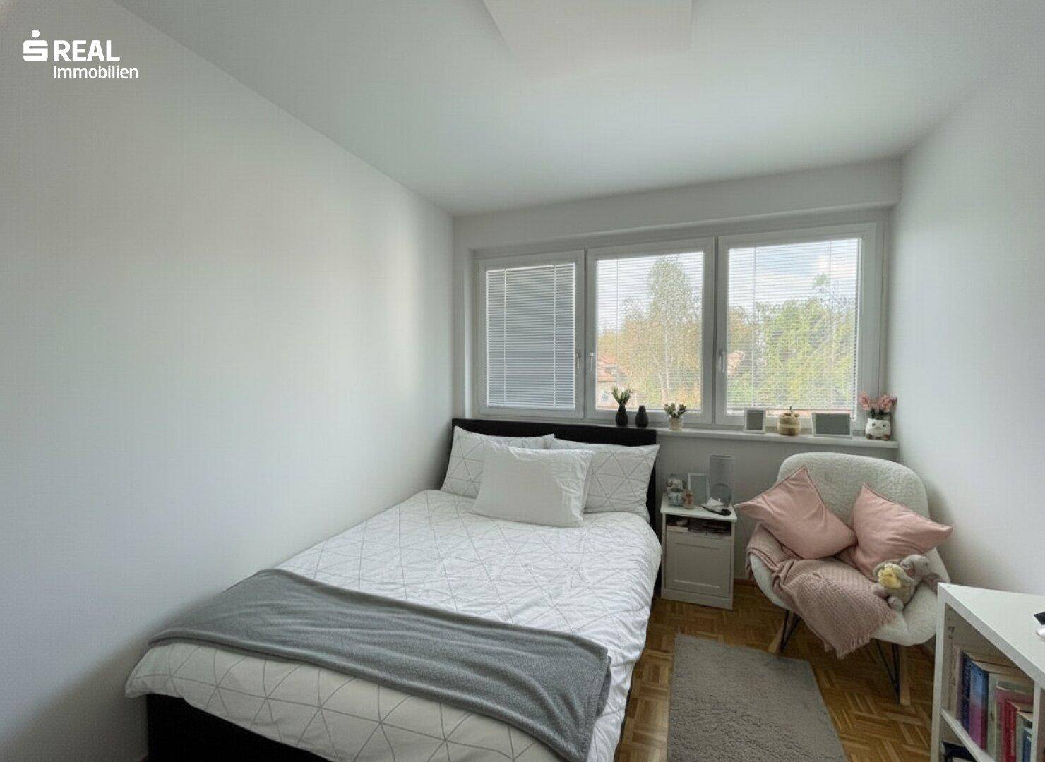 Gemütliches Schlafzimmer mit Einzelbett, Holzboden und Fenster mit Blick ins Grüne.