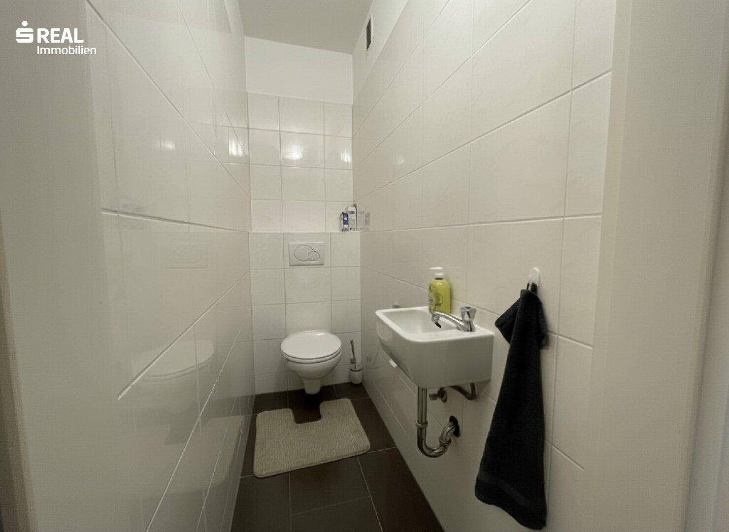 Kleines Gäste-WC mit Wand-WC, Waschbecken und weißen Fliesen.