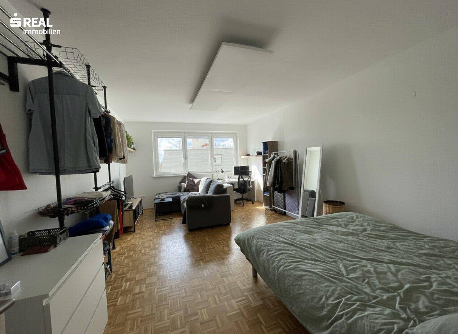 Geräumiges Schlafzimmer mit Doppelbett, Parkettboden und offenem Kleidersystem.