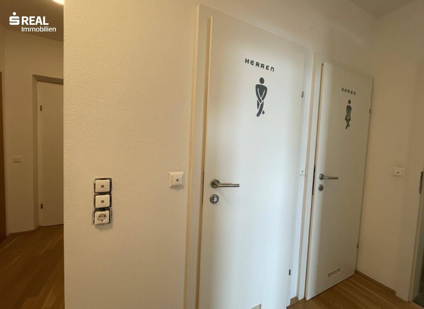 Flurbereich mit zwei Türen, die mit Piktogrammen für Herren und Damen gekennzeichnet sind.