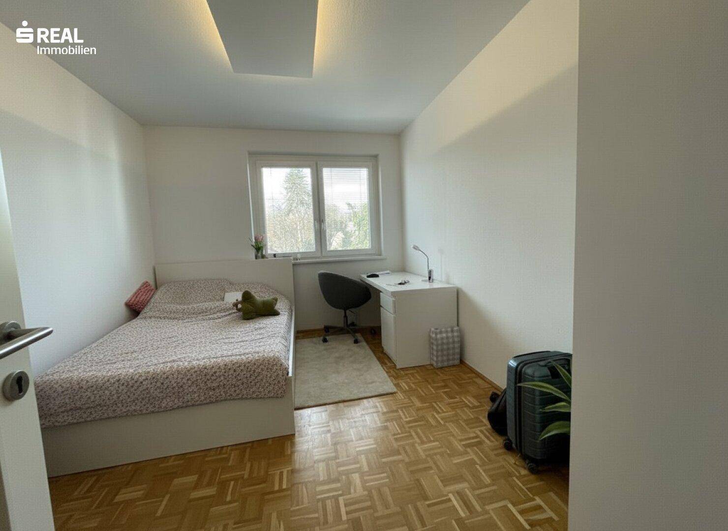 Einfaches Schlafzimmer mit Einzelbett, Schreibtisch und Parkettboden.