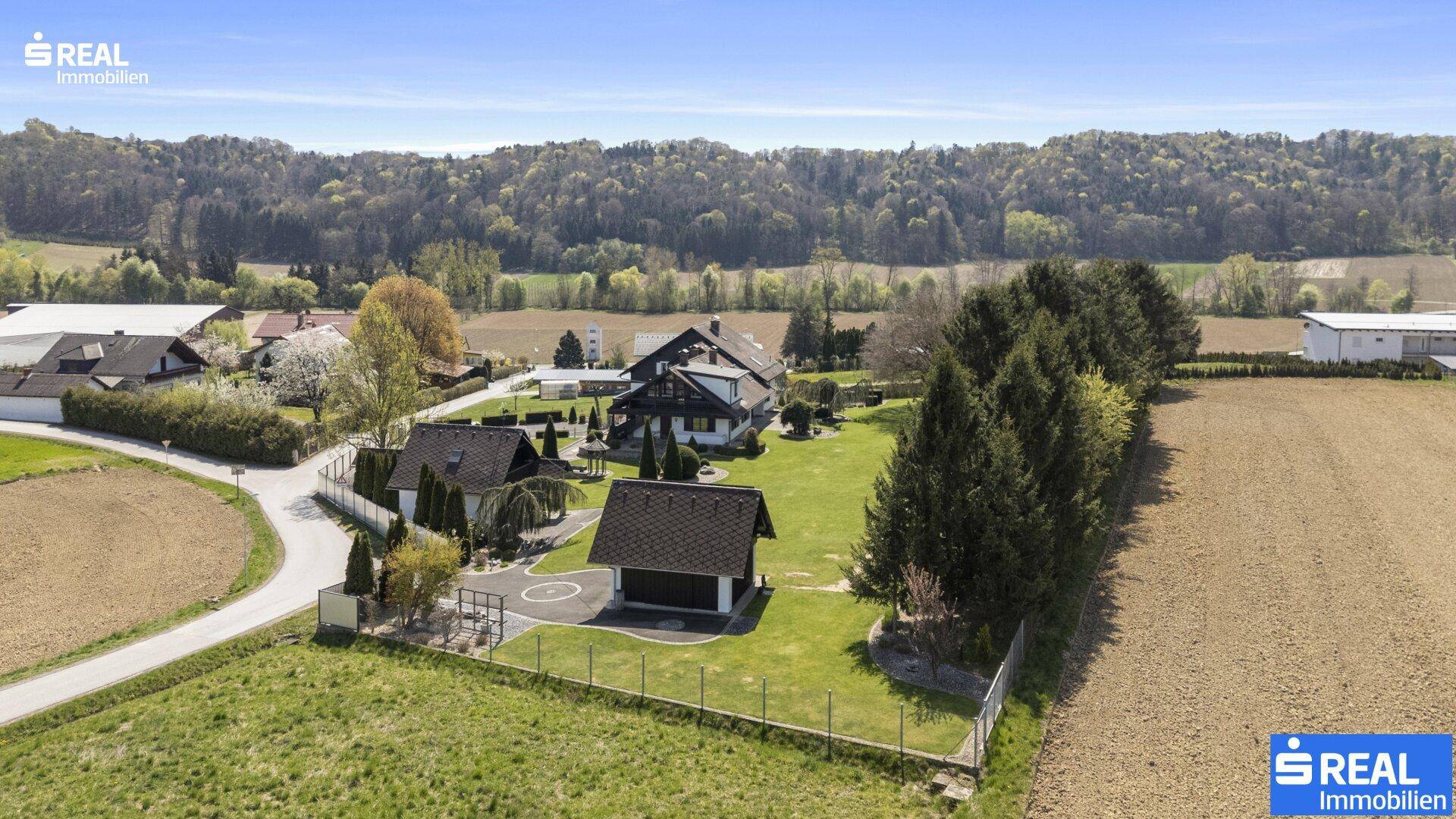 Weitläufiges Anwesen eingebettet in eine ländliche Umgebung mit Feldern und Wald im Hintergrund.