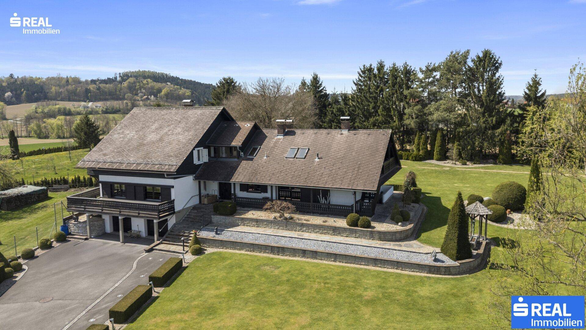 Elegantes Landhaus mit gepflegter Auffahrt und weitläufigem Gartenbereich unter strahlendem Himmel.