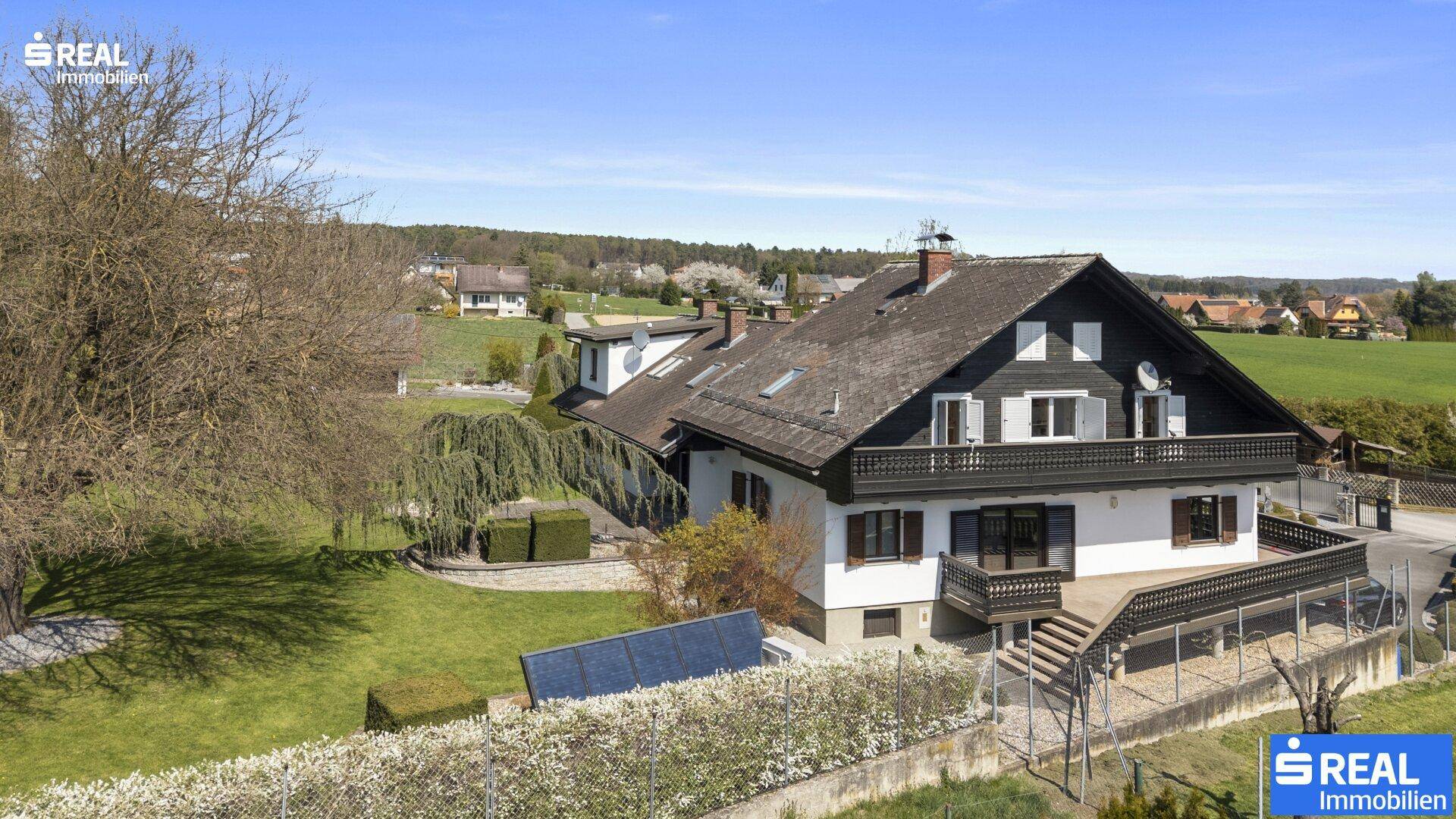 Rückansicht des Hauses mit Balkon und einer am Boden installierten Solaranlage im Garten.
