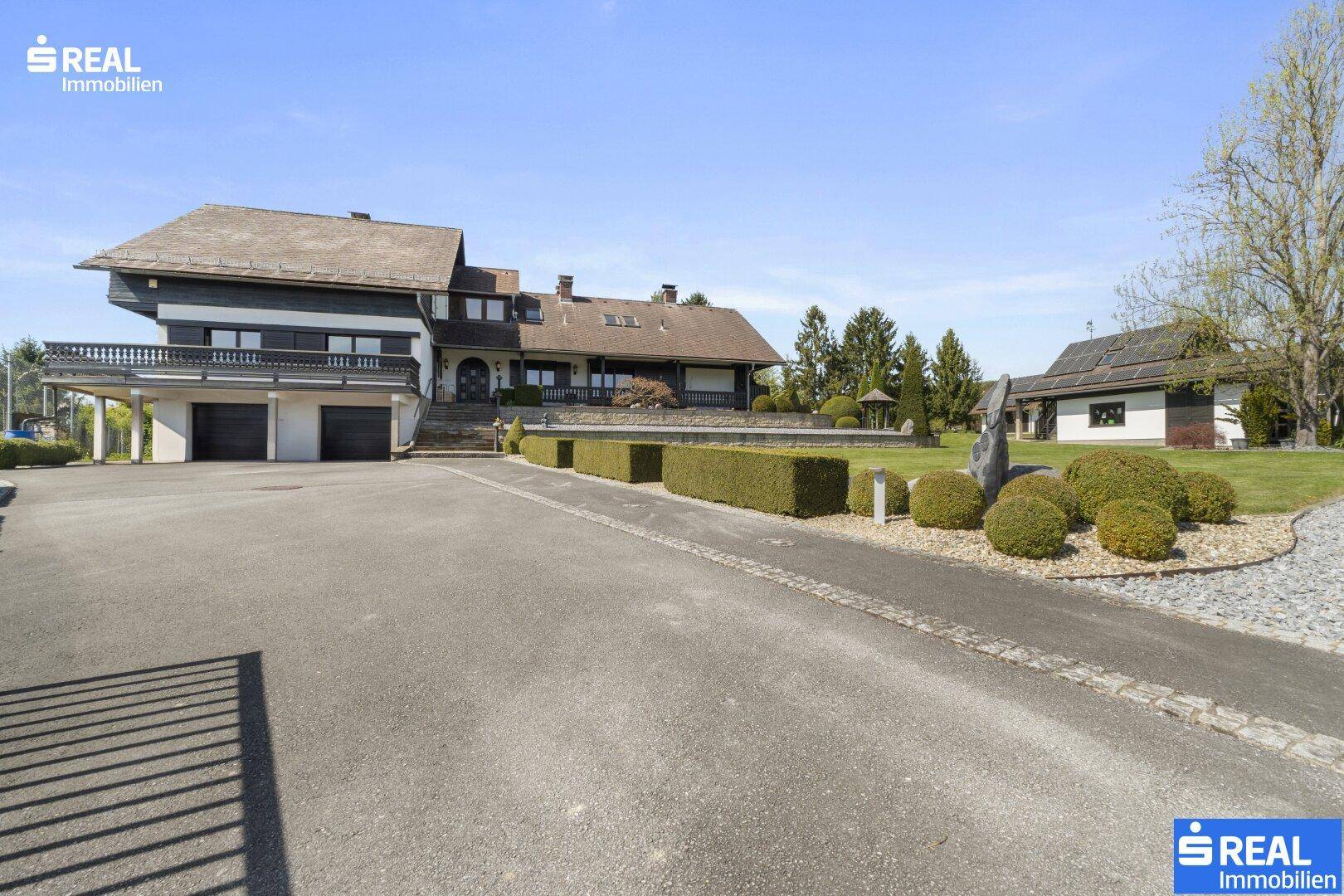 Breite Auffahrt führt zu den Garagen des Hauses, umgeben von gepflegten Hecken und Rasenflächen.