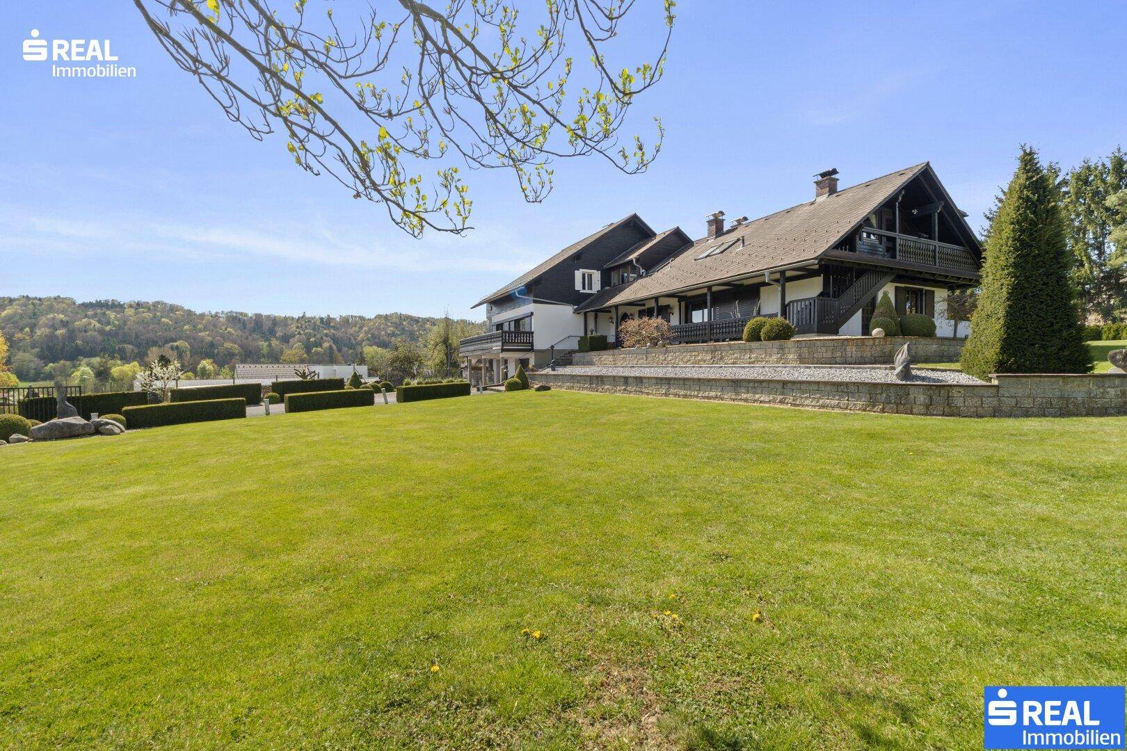 Weitläufige Rasenfläche mit Blick auf das charmante Landhaus und die umliegende Natur.