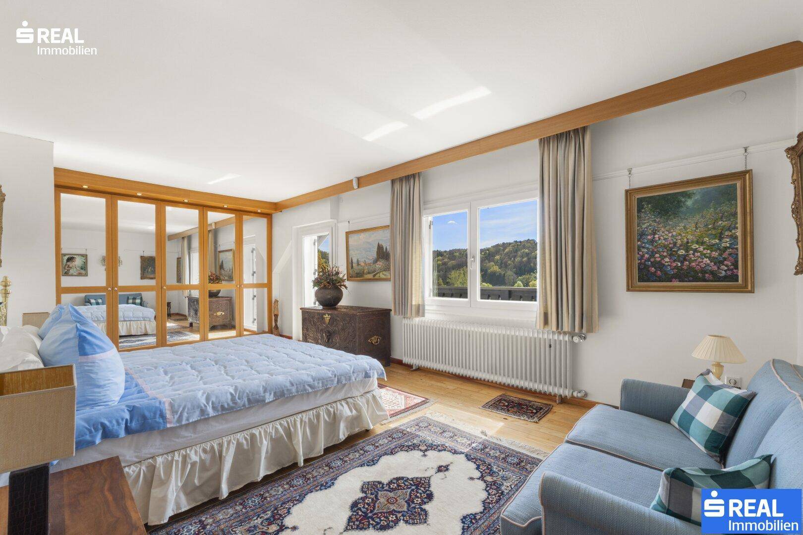 Helles Schlafzimmer mit großem Bett, Sofa, Spiegelschrank und weitem Blick ins Grüne.